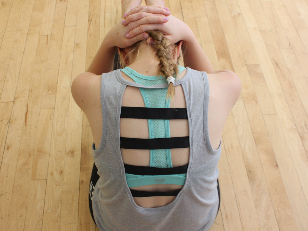 Woman performing Lastics Back Stretch inside on wooden dance floor