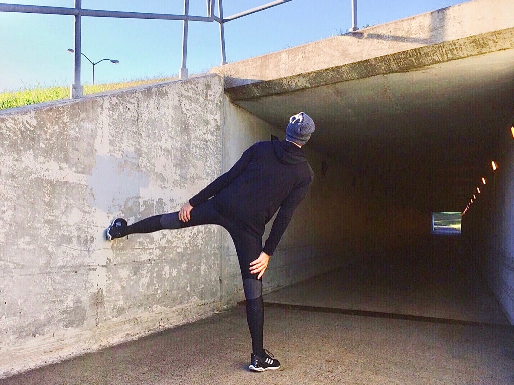 Man in Black with Leg Extended on Concrete Wall to Stretch Tight