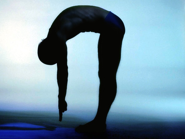 Man in Silhouette on Blue Background in Forward Fold Stretching to Reach Toes